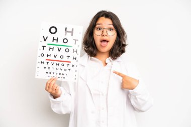 hispanic pretty girl looking surprised and shocked, with jaw dropped holding an object. optical vision test concept