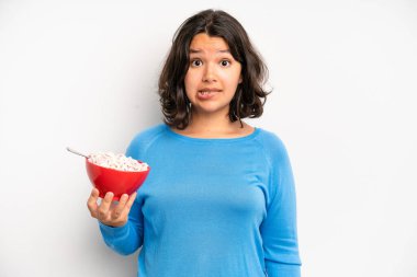 hispanic pretty girl looking surprised and shocked, with jaw dropped holding an object. breakfast concept
