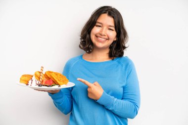 hispanic pretty girl smiling cheerfully, feeling happy and showing a concept. waffles breakfast concept