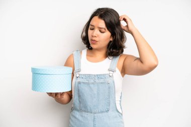 hispanic pretty girl feeling puzzled and confused, scratching head. gift box concept