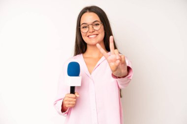 hispanic pretty woma smiling confidently pointing to own broad smile. journalist with a microphone