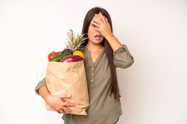 hispanic pretty woma looking unhappy and stressed, suicide gesture making gun sign. market vegetables bag concept