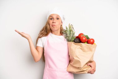 pretty caucasian woman feeling puzzled and confused and doubting. chef with a market vegetables bag