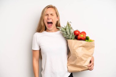 pretty caucasian woman shouting aggressively, looking very angry. chef with a market vegetables bag