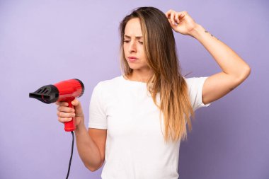 Kafası karışmış, kafası karışmış, kaşınan beyaz bir kadın. saç kurutma makinesi konsepti