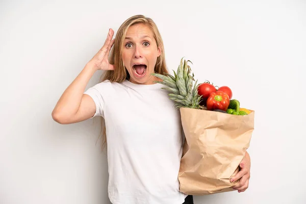 pretty caucasian woman screaming with hands up in the air. chef with a market vegetables bag