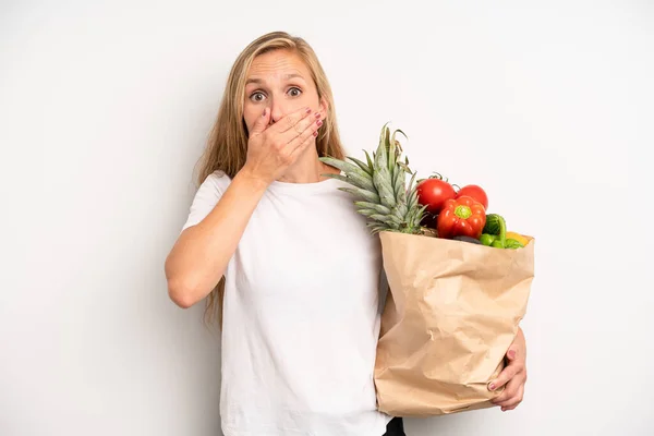 pretty caucasian woman covering mouth with hands with a shocked. chef with a market vegetables bag