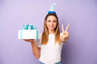 Güzel, beyaz bir kadın gülümsüyor ve arkadaş canlısı görünüyor. İki numarayı gösteriyor. Doğum günü pastası konsepti