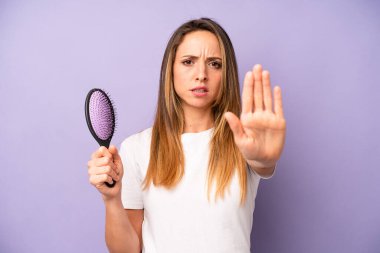 Beyaz kadın ciddi görünüyor. Avuç içinin açık olduğunu gösteriyor. Durdurma hareketi yapıyor. saç tarağı konsepti