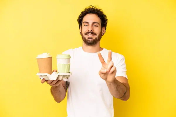 crazy bearded man smiling and looking friendly, showing number two. take away coffee concept