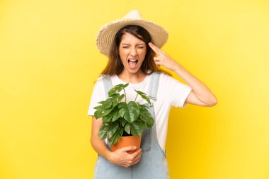 pretty caucasian woman looking unhappy and stressed, suicide gesture making gun sign. gardering concept