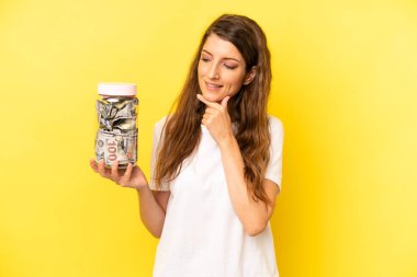 pretty caucasian woman smiling with a happy, confident expression with hand on chin. dollar banknotes savings