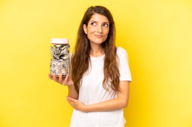 pretty caucasian woman shrugging, feeling confused and uncertain. dollar banknotes savings