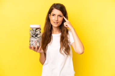 pretty caucasian woman feeling confused and puzzled, showing you are insane. dollar banknotes savings