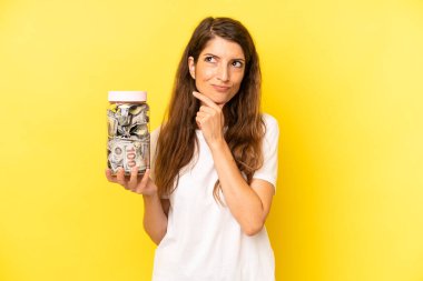 pretty caucasian woman thinking, feeling doubtful and confused. dollar banknotes savings
