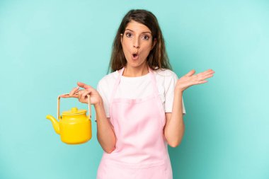 pretty caucasian woman looking surprised and shocked, with jaw dropped holding an object. housewife with a teapot