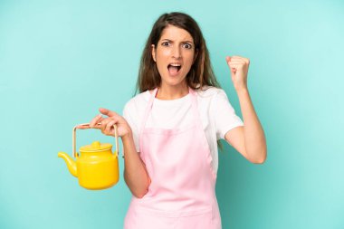 pretty caucasian woman shouting aggressively with an angry expression. housewife with a teapot