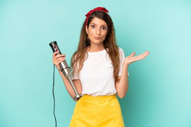 pretty caucasian woman feeling puzzled and confused and doubting. housekeeper with a hand blender
