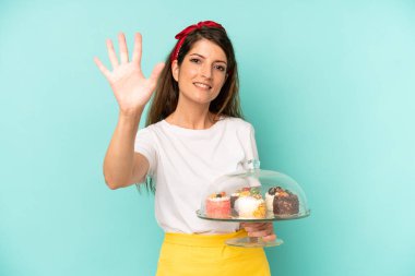 Güzel beyaz kadın gülümsüyor ve arkadaş canlısı görünüyor, beş numarayı gösteriyor. Ev yapımı kek konsepti