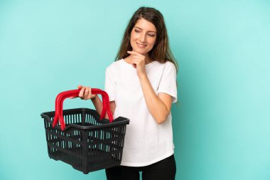 pretty caucasian woman smiling with a happy, confident expression with hand on chin. empty market basket concept