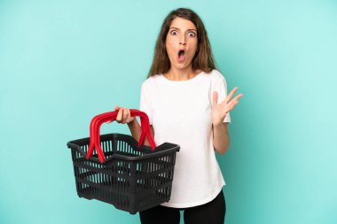 pretty caucasian woman feeling extremely shocked and surprised. empty market basket concept