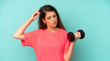 pretty caucasian woman smiling happily and daydreaming or doubting. fitness and dumbbell concept