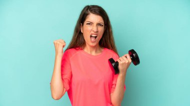 pretty caucasian woman shouting aggressively with an angry expression. fitness and dumbbell concept