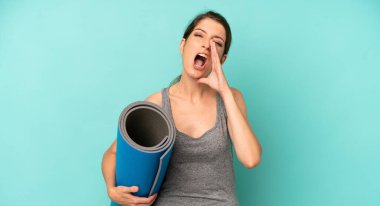 pretty caucasian woman feeling happy,giving a big shout out with hands next to mouth. fitness and yoga concept