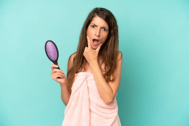 Ağzı ve gözleri açık, eli çenesinde güzel beyaz bir kadın. saç tarağı konsepti