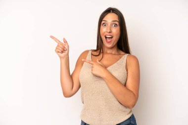 Hispanik güzel kadın neşeli ve şaşırmış hissediyor, şok olmuş bir ifadeyle gülümsüyor ve bir tarafı işaret ediyor.