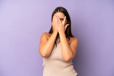 İspanyol güzel kadın elleriyle yüzünü kapatıyor, parmaklarının arasından şaşkın bir ifadeyle yan tarafa bakıyor.