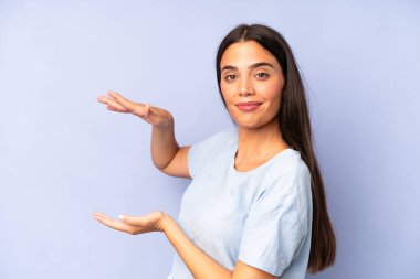 İspanyol asıllı güzel bir kadın bir objeyi iki eliyle fotokopi alanında tutuyor, bir objeyi gösteriyor, sunuyor ya da reklamını yapıyor.