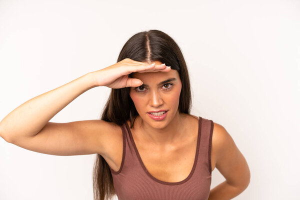 латиноамериканская красивая женщина выглядит озадаченной и изумленной, с рукой над лбом, смотрящей вдаль, смотрящей или ищущей