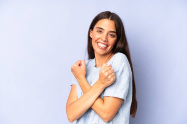 İspanyol güzel kadın neşeli bir şekilde gülümsüyor ve kutluyor, yumruklarını sıkıp kollarını kavuşturuyor, mutlu ve pozitif hissediyor.