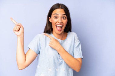 Hispanik güzel kadın neşeli ve şaşırmış hissediyor, şok olmuş bir ifadeyle gülümsüyor ve bir tarafı işaret ediyor.