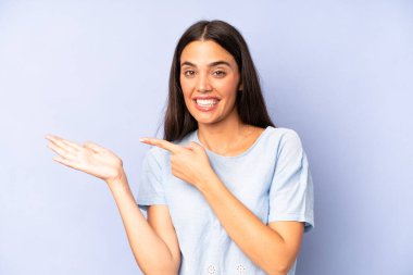 İspanyol güzel kadın neşeyle gülümsüyor ve yan taraftaki fotokopi alanını işaret ediyor, bir nesneyi gösteriyor ya da reklamını yapıyor.