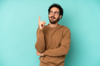 Genç sakallı adam mutlu bir şekilde gülümsüyor ve yan bakıyor, merak ediyor, düşünüyor ya da bir fikri var.