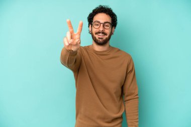 Genç sakallı adam gülümsüyor ve mutlu görünüyor, kaygısız ve pozitif, zafer ya da barışı simgeliyor.