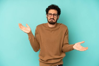 Genç sakallı adam şaşkın, kafası karışmış ve stresli görünüyor, farklı seçenekler arasında merak ediyor, kararsız hissediyor.