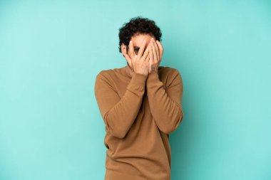 Genç sakallı adam elleriyle yüzünü kapatıyor, parmaklarının arasından şaşkın bir ifadeyle yan tarafa bakıyor.