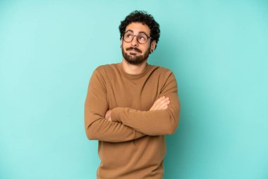 Genç sakallı adam omuz silkiyor, kafası karışık ve emin değil, kolları bağlı ve şaşkın görünüyor.