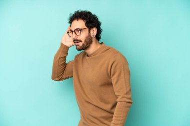 Genç sakallı adam gülümsüyor, tuhaf bir şekilde yan tarafa bakıyor, dedikoduları dinlemeye ya da bir sırrı duymaya çalışıyor.