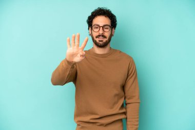 Genç sakallı adam gülümsüyor ve arkadaş canlısı görünüyor. Elleri önde, geriye doğru sayıyor.