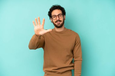 Genç sakallı adam gülümsüyor ve arkadaş canlısı görünüyor. 5 ya da 5 numarayı gösteriyor.