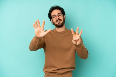 Genç sakallı adam gülümsüyor ve arkadaş canlısı görünüyor, 8 ya da 8 numarayı gösteriyor, elleri önde, geriye doğru sayıyor.