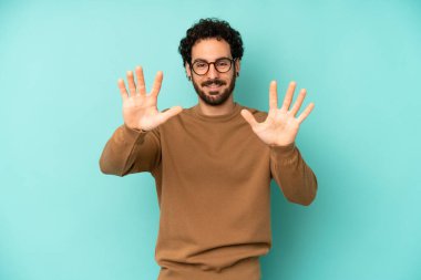 Genç sakallı adam gülümsüyor ve arkadaş canlısı görünüyor, onuncu veya onuncu numarayı gösteriyor, eli önde, geriye doğru sayıyor.