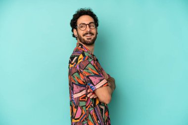 Genç sakallı adam neşeyle gülümsüyor, mutlu, tatmin olmuş ve rahatlamış hissediyor, kollarını kavuşturup yan tarafa bakıyor.