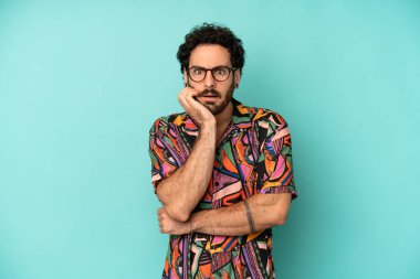 Genç sakallı adam şok ve inançsızlıkla ağzı açık, elleri yanağında ve kolları çaprazlanmış, sersemlemiş ve şaşırmış hissediyor