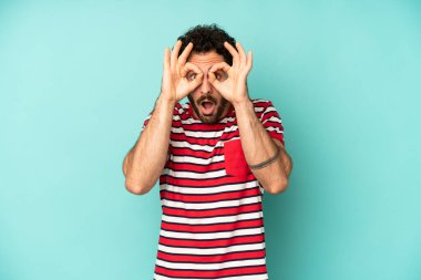 Genç sakallı adam şaşkın, şaşırmış ve şaşırmış hissediyor, elinde şaşkın, inançsız bir bakışla gözlük tutuyor.