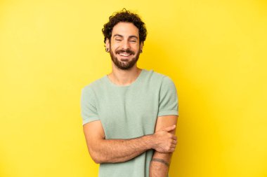 Genç sakallı adam utangaç ve neşeli bir şekilde gülüyor, arkadaş canlısı ve olumlu ama güvensiz bir tavırla.